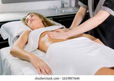 Side angle view of hands massaging female abdomen. Therapist applying pressure on belly. Pretty young blond woman receiving manual massage at spa salon