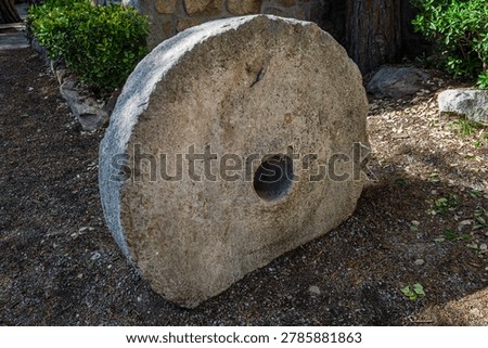 Side angle view of a massive ancient stone millstone resting on the earth, ideal for historical agriculture and heritage designs.