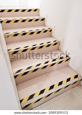 Side angle view of staircase with yellow and black stripes warning sign sticker. Safety and prevention concept.