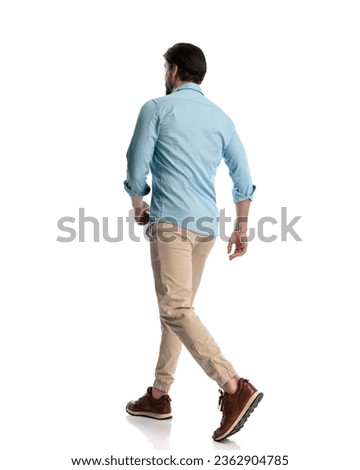 side and back view of casual young man in denim shirt with chino pants and sneakers walking in front of white background