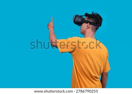 Side Back View of Man Wearing Virtual Reality Goggles and Pointing His Finger up, Isolated on Vibrant Blue Background