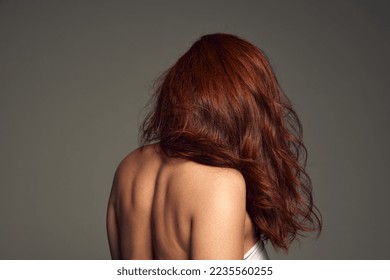 Side , back view portrait of young woman with perfect hair, deep red color and mega volume over grey background. Colorist, hair dying. Concept of beauty, hair treatment, cosmetics, care. Ad, poster