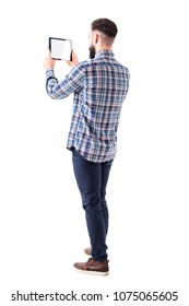 Side Back View Of Young Business Bearded Man Holding Pad Tablet Computer Taking Photo. Blank Screen. Full Body Isolated On White Background.