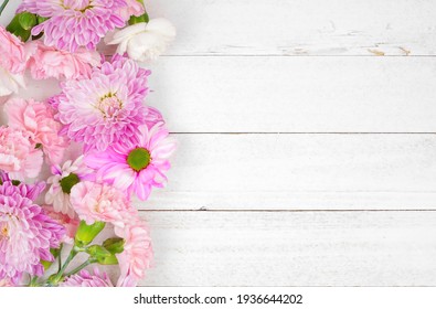 Side border of pink and purple flowers with mums, daisies and carnations against a white wood background. Copy space.