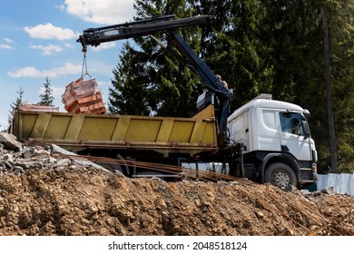 Side Bottom Pov Big Modern Truck With Mounted Self Loading Crane Arm Boom Unloading Pallet Of New Bricks At Countryside Rural Forest Suburban Construction Site. Building Materials Delivery Service.