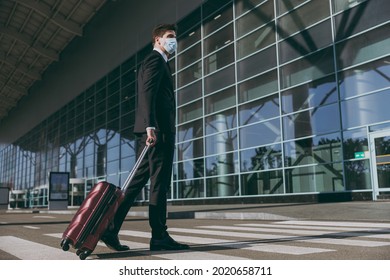 Side Bottom View Full Body Young Traveler Businessman Man In Black Suit Facial Mask Walk Go Outside At International Airport Terminal With Suitcase Valise Cross Road Air Flight Business Trip Concept