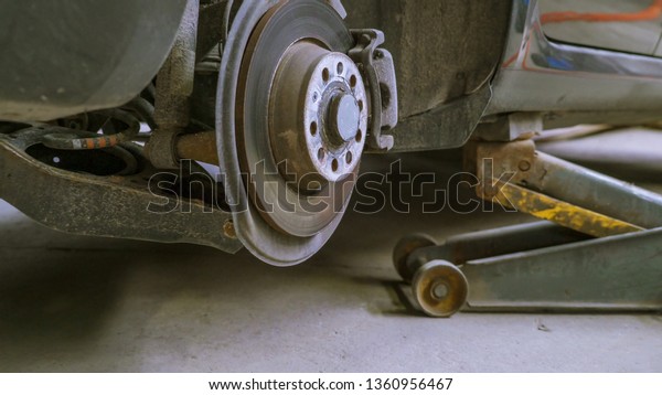 The side of the car with\
no tire inside the auto shop with the jack and screws on the\
floored scattered
