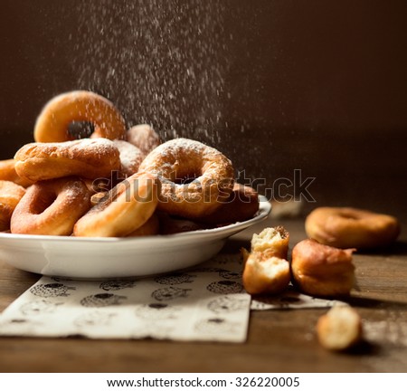 Side close up on a bunch of fresh homemade donuts (doughnuts) with sugar, on a white plate, light napkins on a dark wooden floor 
