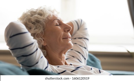 Side close up view face serene 60s woman closed eyes put hands behind head enjoy fresh air, leaned on sofa replenish strength looking calm, repeats in head affirmations, makes positive mood concept