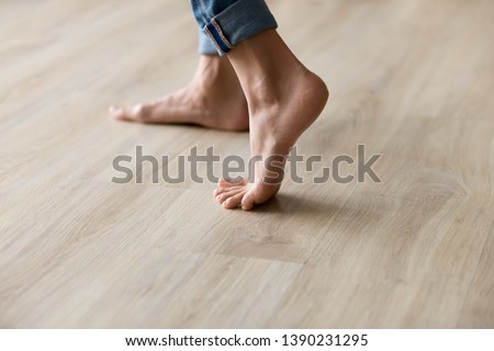 Side close up view of unrecognizable woman feet legs, barefoot girl standing indoors inside of modern home enjoy warm wooden heated floor, perfect groomed body part pedicure services spa salon concept
