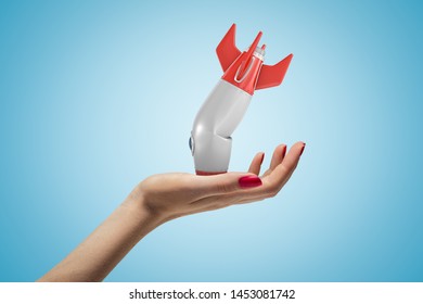 Side closeup of woman's hand facing up and holding small broken rocket upside down, on light blue gradient background. Space programs. Technical fault. Problems and malfunction. - Powered by Shutterstock