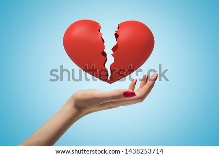 Side closeup of woman's hand facing up and levitating red broken heart on light blue gradient background. Love and relationship. Feelings and emotions. Breaking-up.
