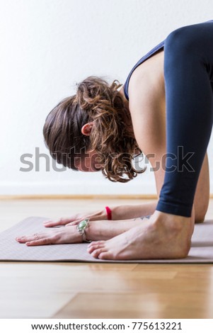 Side detail view of a young woman in her early 30's, with her hands and left foot near her face, while she performs an asana or yoga pose in her home during her daily practice