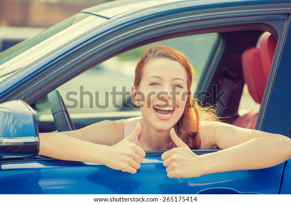 Side door view woman driver happy smiling\
showing thumbs up sitting inside new blue car  outside on parking\
lot background. Beautiful young woman happy with her new vehicle.\
Positive face expression