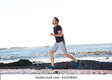 Side Full Body Portrait Of Active Man Running By Beach