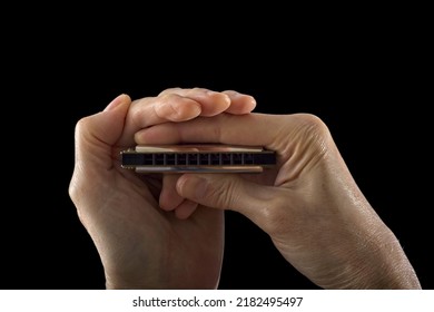 Side lit harmonica held in two hands in front of dark background.