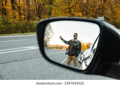 In the side mirror of the car behind the autumn trees was a hitchhiker looking for a ride