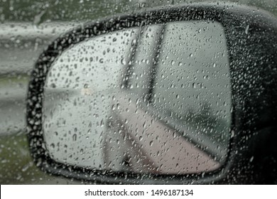 Side mirror of a car with raindrops. Safety on the road. Bad visibility. Defocused background. Mirror reflects the asphalt wet road.