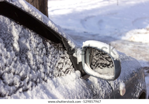 Side mirror\
of the car in the snow. Fragment of the car with side doors, wing,\
mirror covered with snow.  Sunny\
day.