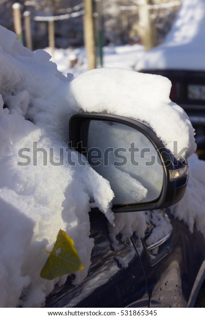 Side mirror of the\
car in the snow. Fragment of the car with side doors, mirror\
covered with snow.  Sunny\
day.