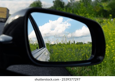 The side mirror reflects a bright green field with yellow wildflowers and fluffy clouds against a blue sky on a sunny day. - Powered by Shutterstock