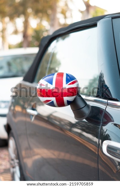 Side\
mirror with the United Kingdom flag. Car parked in the street with\
the UK flag on the rear view mirror. Reflections of light on the\
bodywork and windows of a car parked in the\
street.
