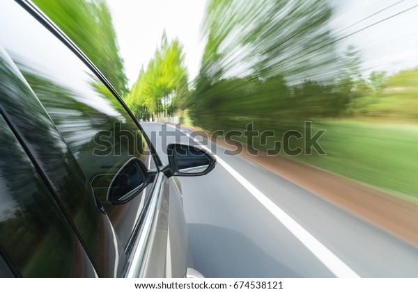 side mirror view of car driving with\
trees on both sides of the road, fast motion\
blur