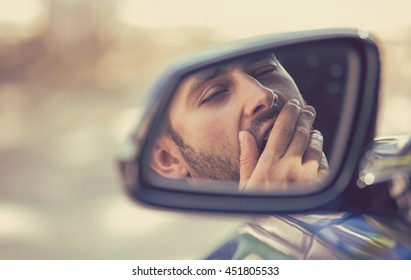 Side mirror view reflection sleepy tired fatigued yawning exhausted young man driving his car in traffic after long hour drive. Transportation sleep deprivation accident concept
