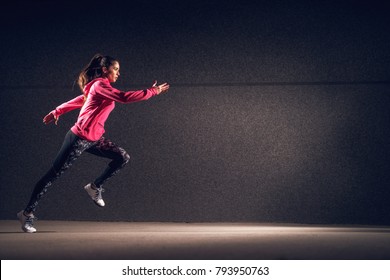 Side Motion View Of Young Sexy Attractive Healthy Fitness Sporty Active Slim Girl With Sportswear Running In Front Of The Grey Wall At Night On The Street.