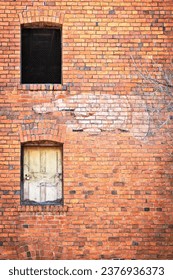 Side of an old brick building with two windows, one empty and one boarded, with a faded old sign of a finger pointing