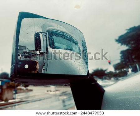 Side outer mirror mounted on big rig heavy tractor trailer truck reflecting the truck cabin on rainy morning