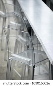 Side Overhead Close Up On A Row Of Clear Plastic Acrylic Bar Stool Chairs, Along A Counter Top, At A Modern Restaurant