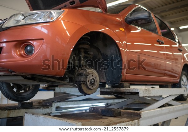 Side part of\
broken car of light brown color without one wheel standing in\
workshop to get checked and\
repaired