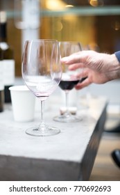 Side perspective close up on an empty wine glass with red wine dregs with a hand reaching for  another glass in the blurry background