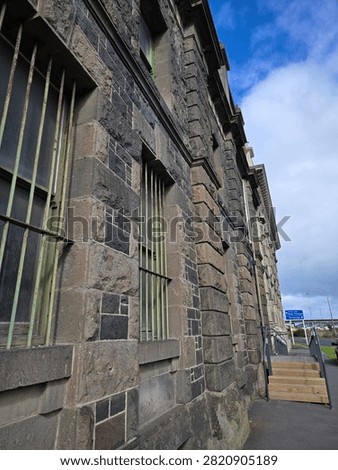 A side perspective of a dark bluestone historical building exterior with barred windows in Dunedin, South Island, New Zealand.