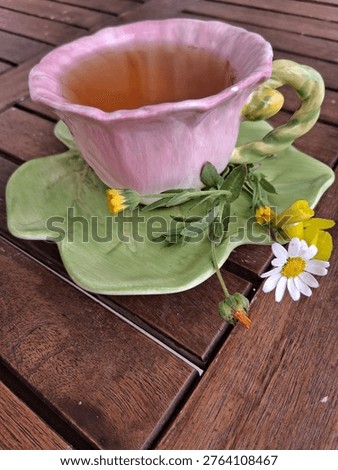 Side perspective of a single pink tea cup resembling a flower, filled with green tea and decorated with wildflowers.