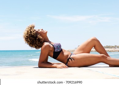 Side portrait of attractive black woman lying on the beach and sunbathing