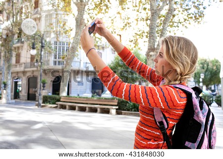 Side portrait of a college student holding a smart phone, taking pictures of a destination city on holiday, sunny outdoors. Travel lifestyle and technology. Young woman using cell phone, exterior.