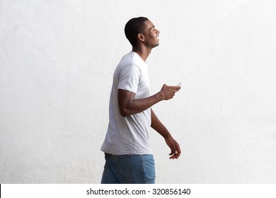 Side portrait of a cool black guy walking with cell phone against white wall - Powered by Shutterstock