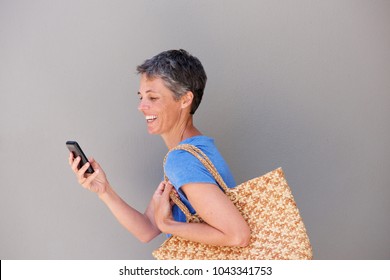 Side Portrait Of Happy Middle Aged Woman Walking And Looking At Mobile Phone