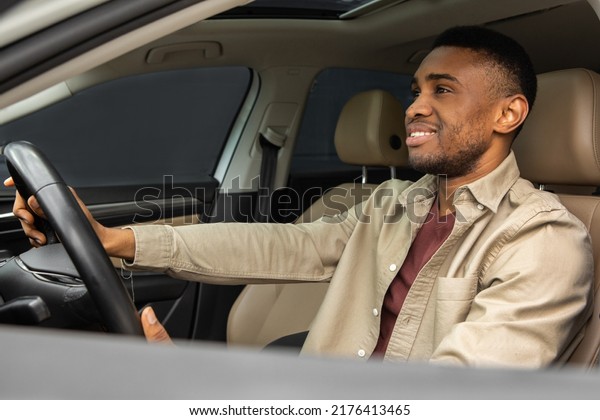 Side portrait of happy young black male driver\
driving a car
