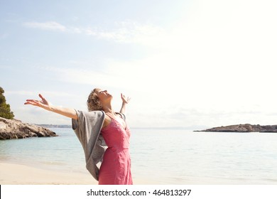 Side Portrait Of A Mature Beautiful Woman Breathing Fresh Air In A Beach Destination With Blue Waters, Opening Her Arms And Looking Up, Aspirational Travel Lifestyle, Outdoors Nature.