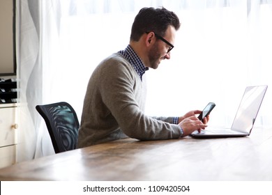 Side Portrait Of Older Man Working At Home With Laptop And Mobile Phone