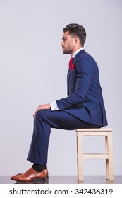 Side Portrait On Man In Suit Sitting In Studio With Hands On His Knees