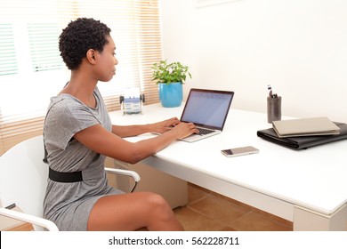 Portrait parallèle d'une afro-américaine professionnelle travaillant à domicile, utilisant un ordinateur portable, à l'intérieur. Femme d'affaires noire au bureau avec écran vierge, travaillant à la maison, à l'intérieur.