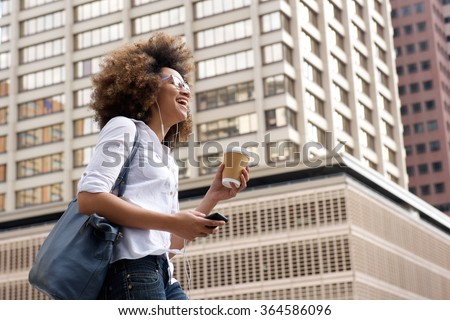 Side portrait of a smiling african american woman walking in the city with cellphone