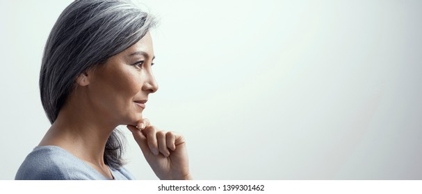 Side Portrait Of Smiling Asian Woman With Grey Hair Touching The Chin. Beautiful Middle-Aged Woman In Profile Touching Chin