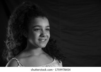 Side portrait of smiling teenage girl without looking at the camera with black background and curly hair. Black and white horizontal image. Concept of emotions.