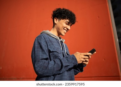 Side portrait smiling young man using mobile phone by red wall - Powered by Shutterstock