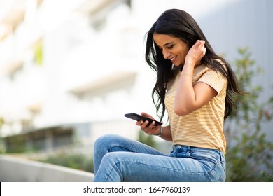 Side Portrait Smiling Young Woman Sitting Outside Looking At Mobile Phone